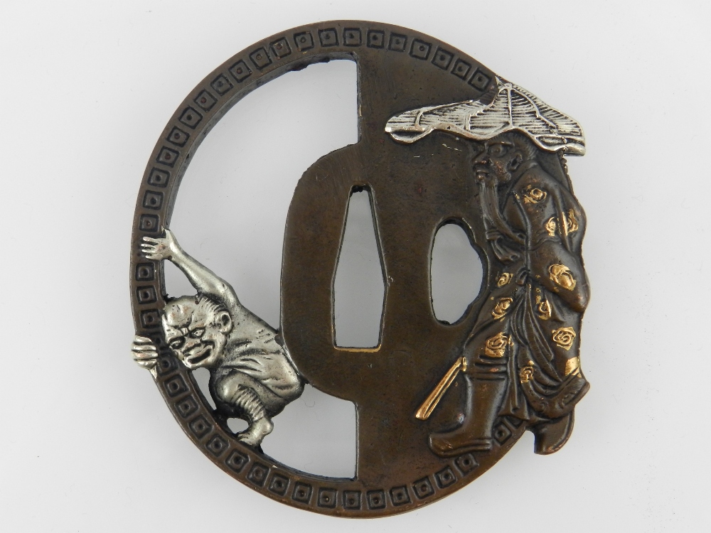 A Japanese cast bronze Katana Tsuba, decorated with an elderly man and a devil, bears script to