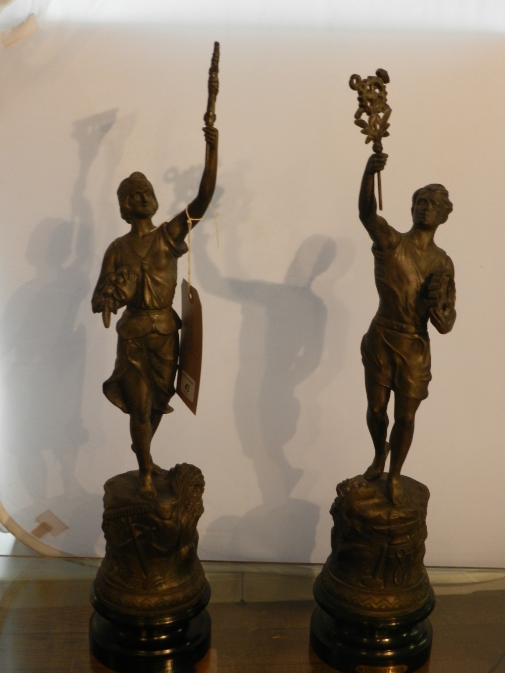 A pair of late 19th century French spelter figures, 'L'industrie' and one other, each raised on