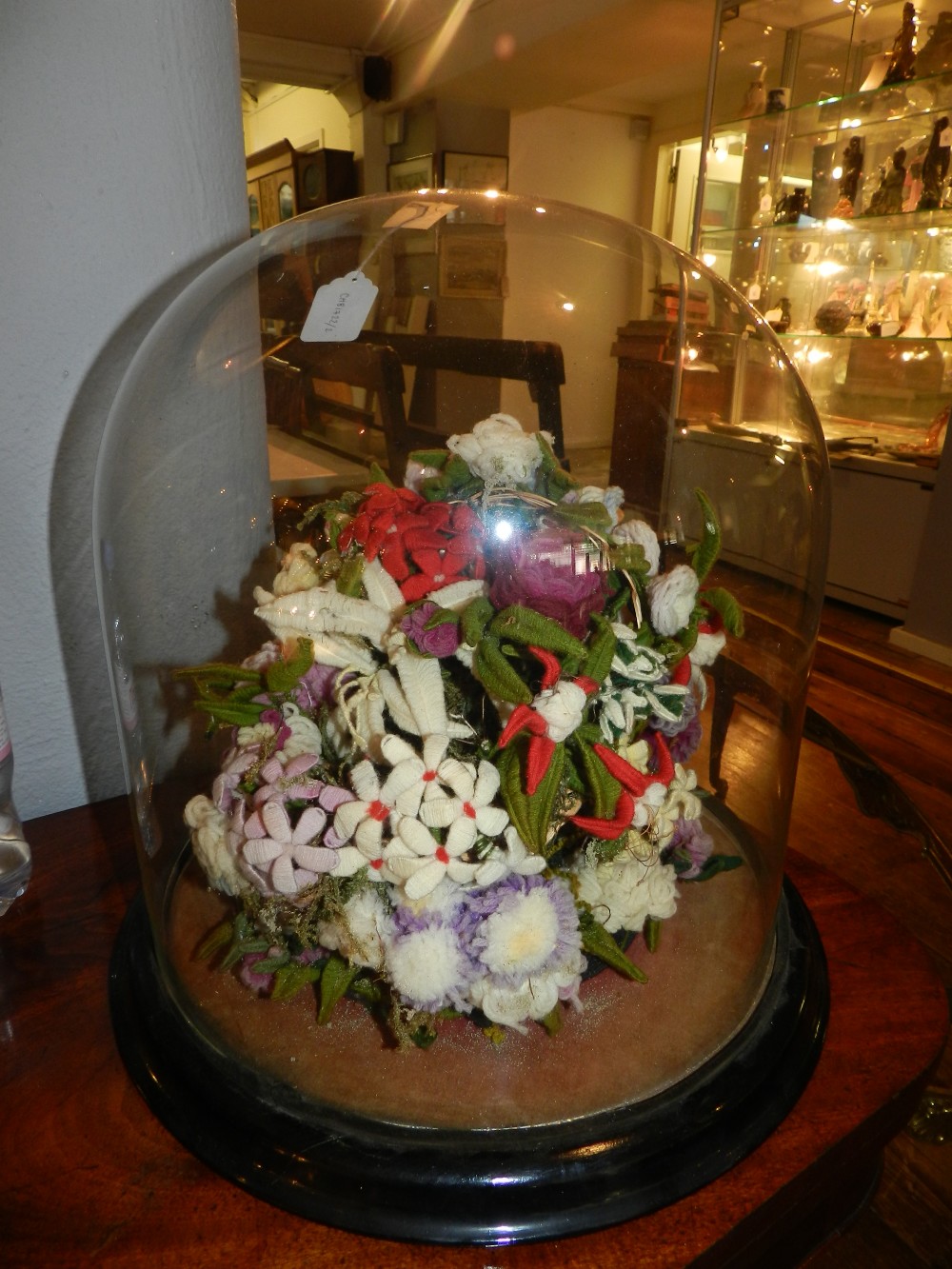 A Victorian mixed media woolwork and wire floral arrangement within a glass dome, raised on a