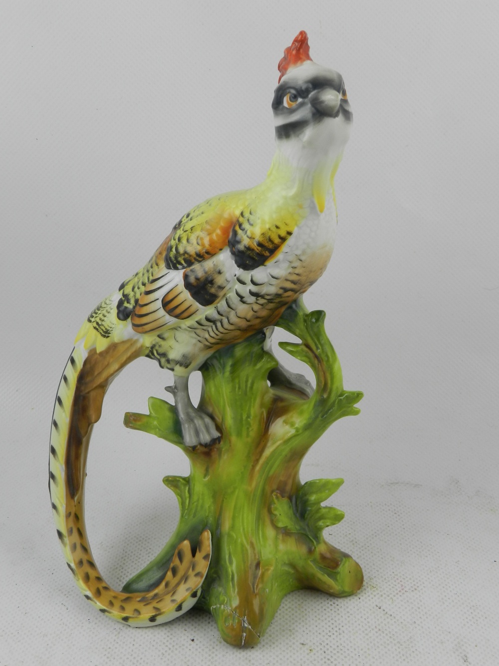 A mid 20th century German hard paste porcelain study of an exotic bird, raised on a tree stump. H: