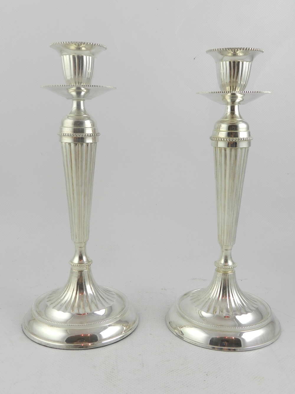 A pair of silver plated candle holders, raised tapered reeded columns on a circular foot. H.24.5cm