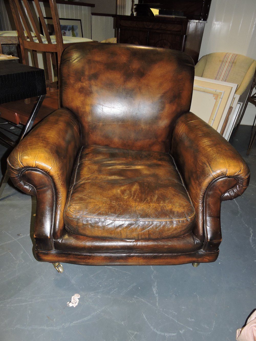 A late Victorian style aged brown leather club armchair with scroll arms and loose cushion seat on