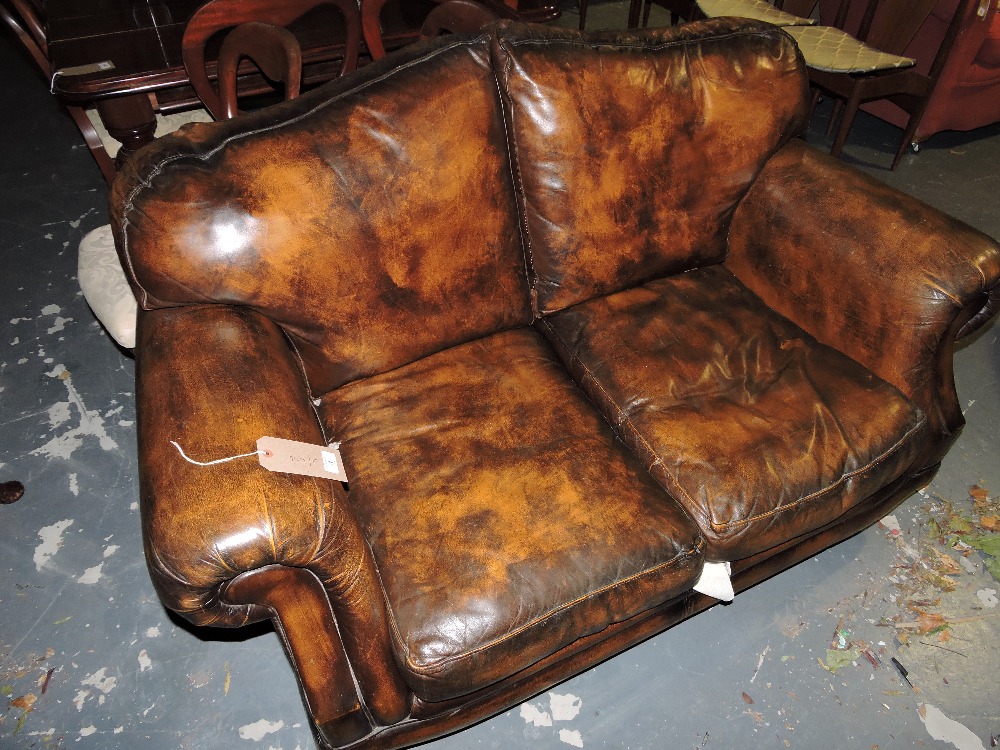 A late Victorian style aged brown leather sofa with scroll arms and loose cushion seat on turned