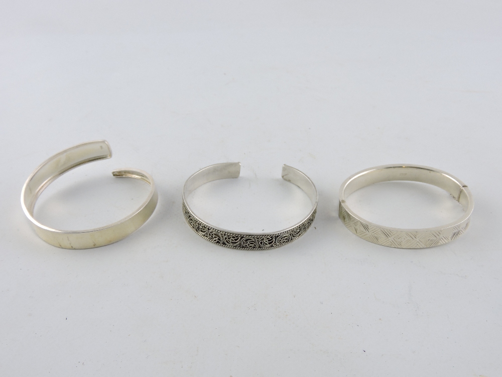 An engraved silver hinged bangle together with two further silver bangles.