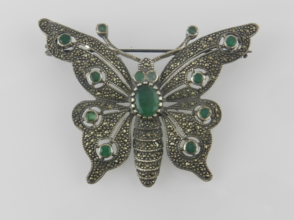 An early 20th century silver butterfly pin brooch set with semi precious green stones on a marcasite