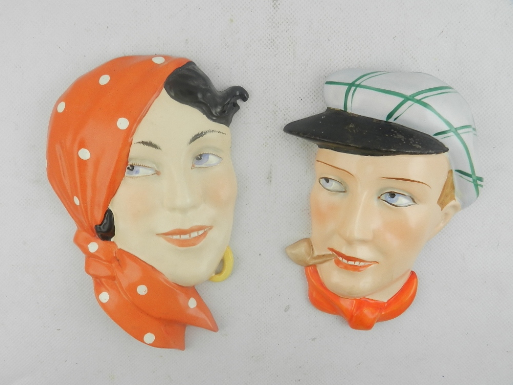 Two Continental Art Deco ceramic wall masks of a young gentleman in a sporting cap smoking a pipe,