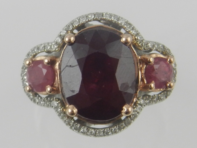 A white metal, ruby and diamond dress ring, set central faceted stone flanked by two smaller, within