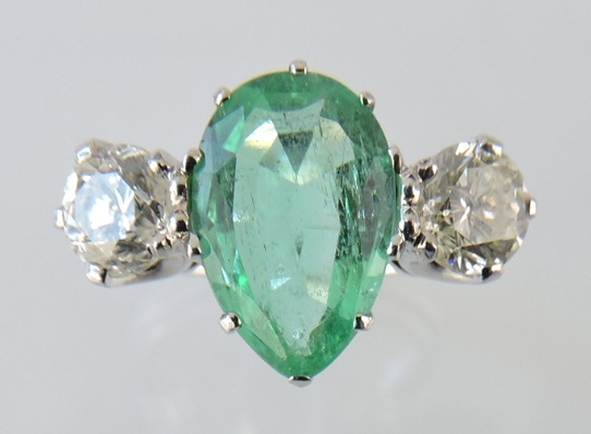 An emerald and diamond dress ring, the pear-shaped central emerald of approx. 2.5ct, flanked by