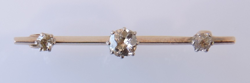 A three-stone diamond bar brooch, the central stone approx. 0.33ct, on a yellow metal bar, flanked