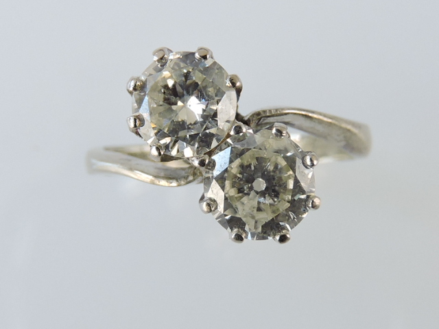 A two stone cross-over diamond ring, each stone of approx. 1ct, claw set in a white metal band