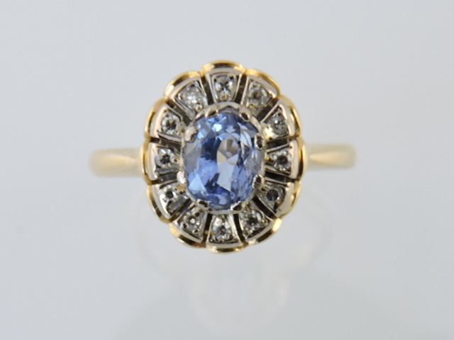 A sapphire and diamond dress ring, the cornflower blue oval stone set within a border of diamonds on