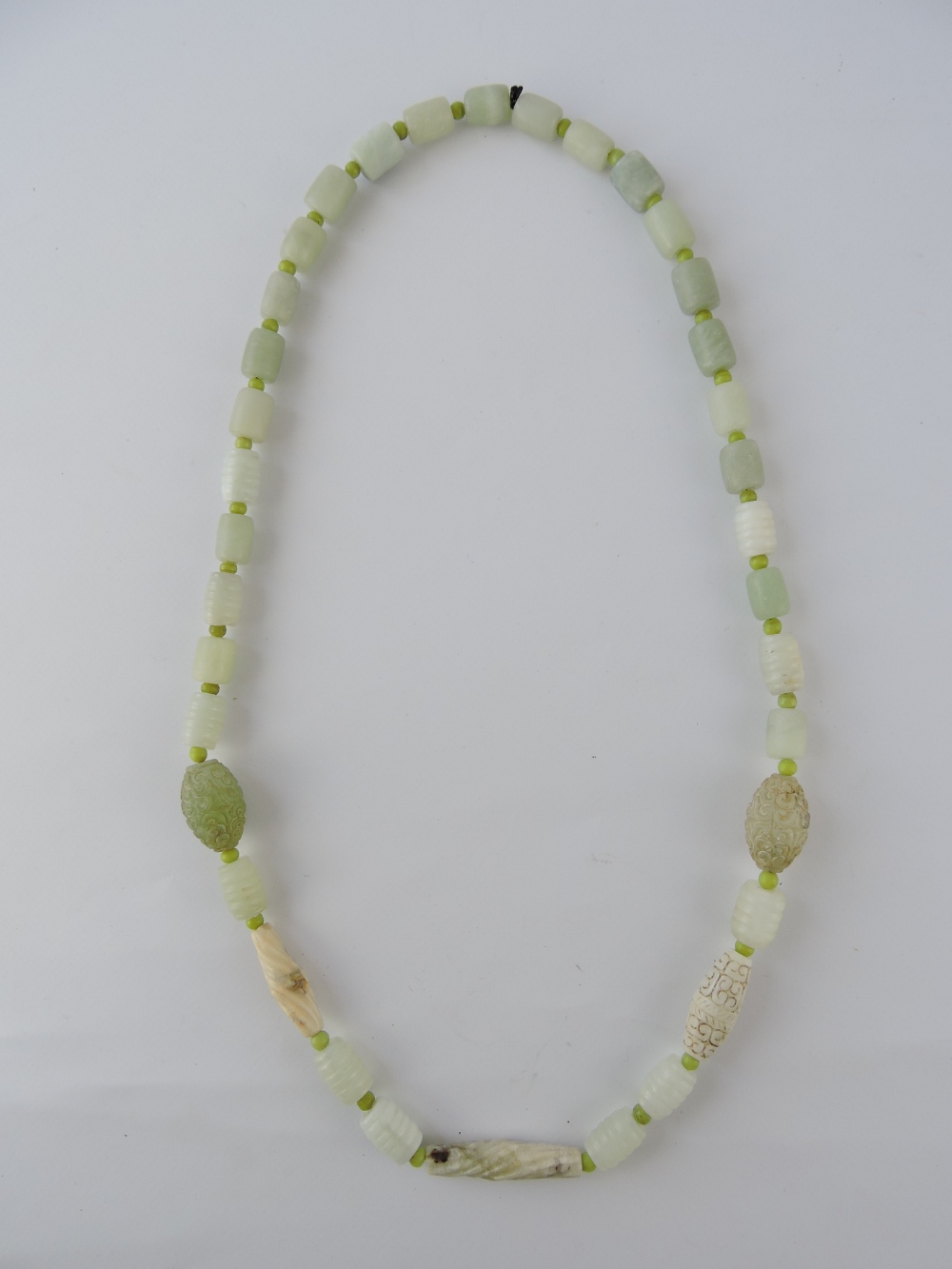 A jade necklace, constructed barrel-shaped beads including two oval carved beads, L. 80cm.