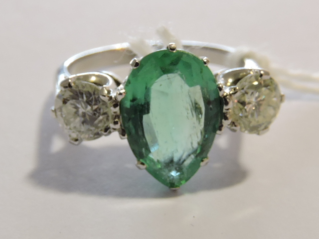 An emerald and diamond dress ring, the pear-shaped central emerald of approx. 2.5ct, flanked by