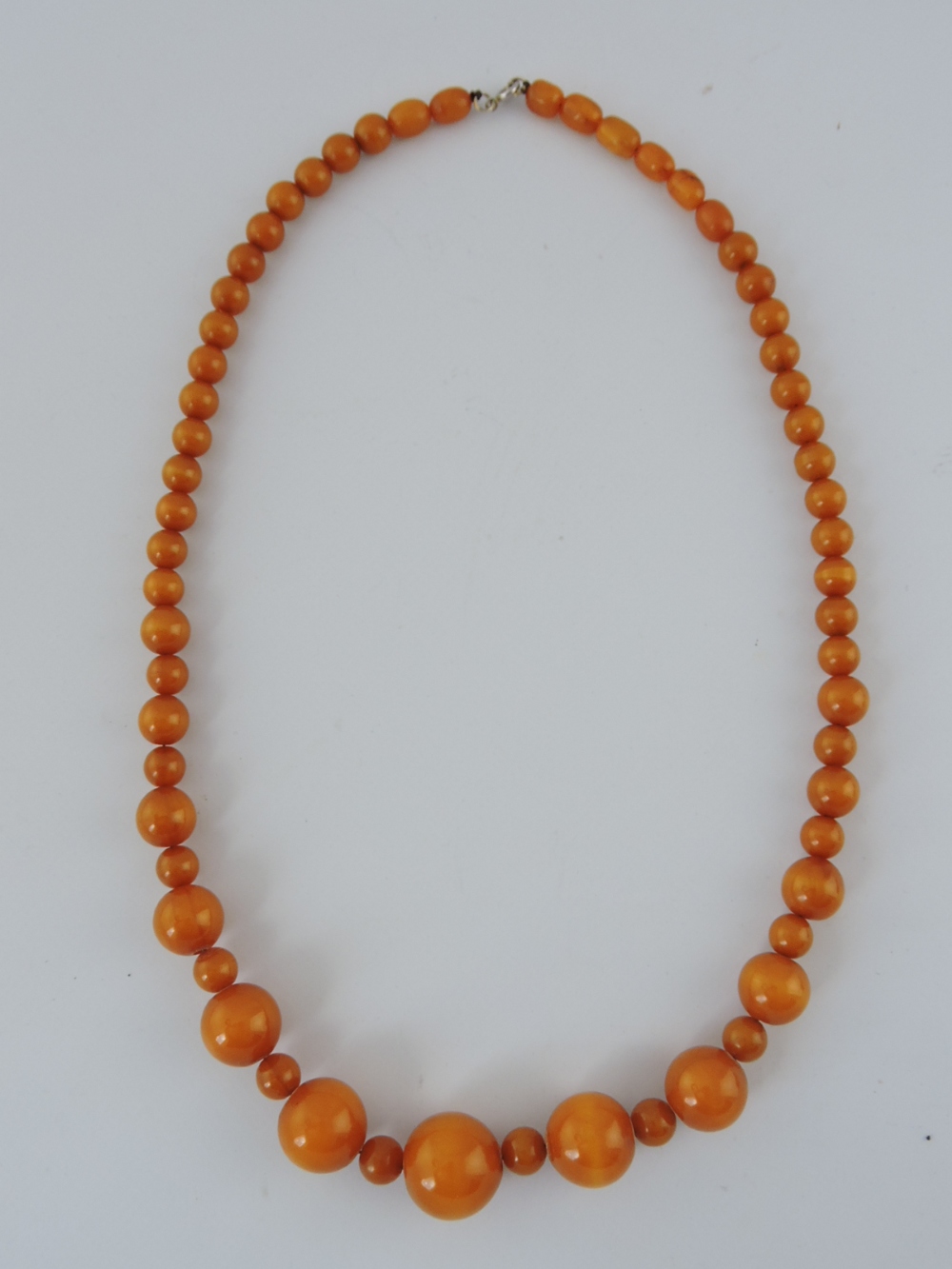 An amber necklace of graduated beads, including nine oversize beads, L. 83cm.