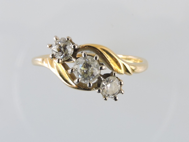 A three-stone diamond ring, set in a yellow metal band marked 18ct, 3.2g.