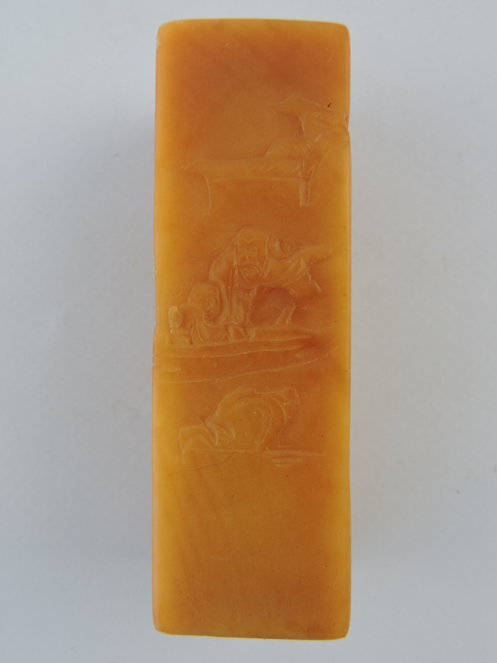 A honey coloured soapstone seal, carved with figures in a mountainous landscape.