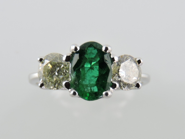 A three-stone emerald and diamond ring, claw set in an 18ct white gold band.