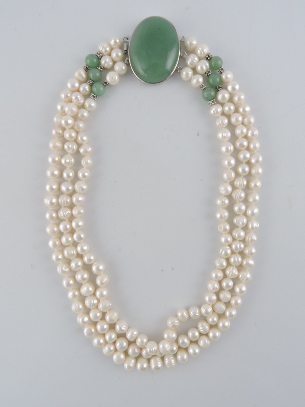 A three-row string of natural pearls, with a large oval jade clasp and six jade beads, approx. L.