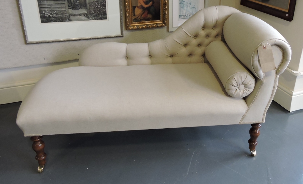 A Victorian style small chaise longue, upholstered in buttoned natural fabric, on turned legs with