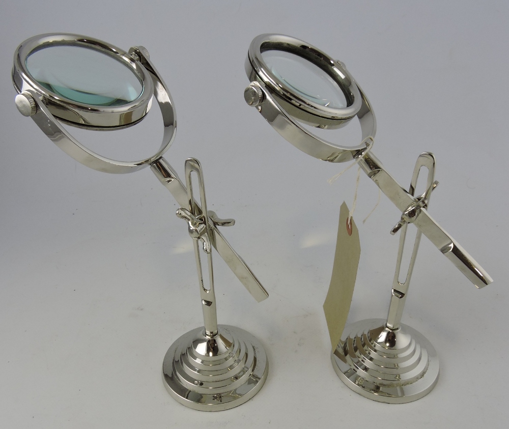 A pair of white metal magnifying glasses on adjustable stands, on circular stepped bases, H. 36cm.