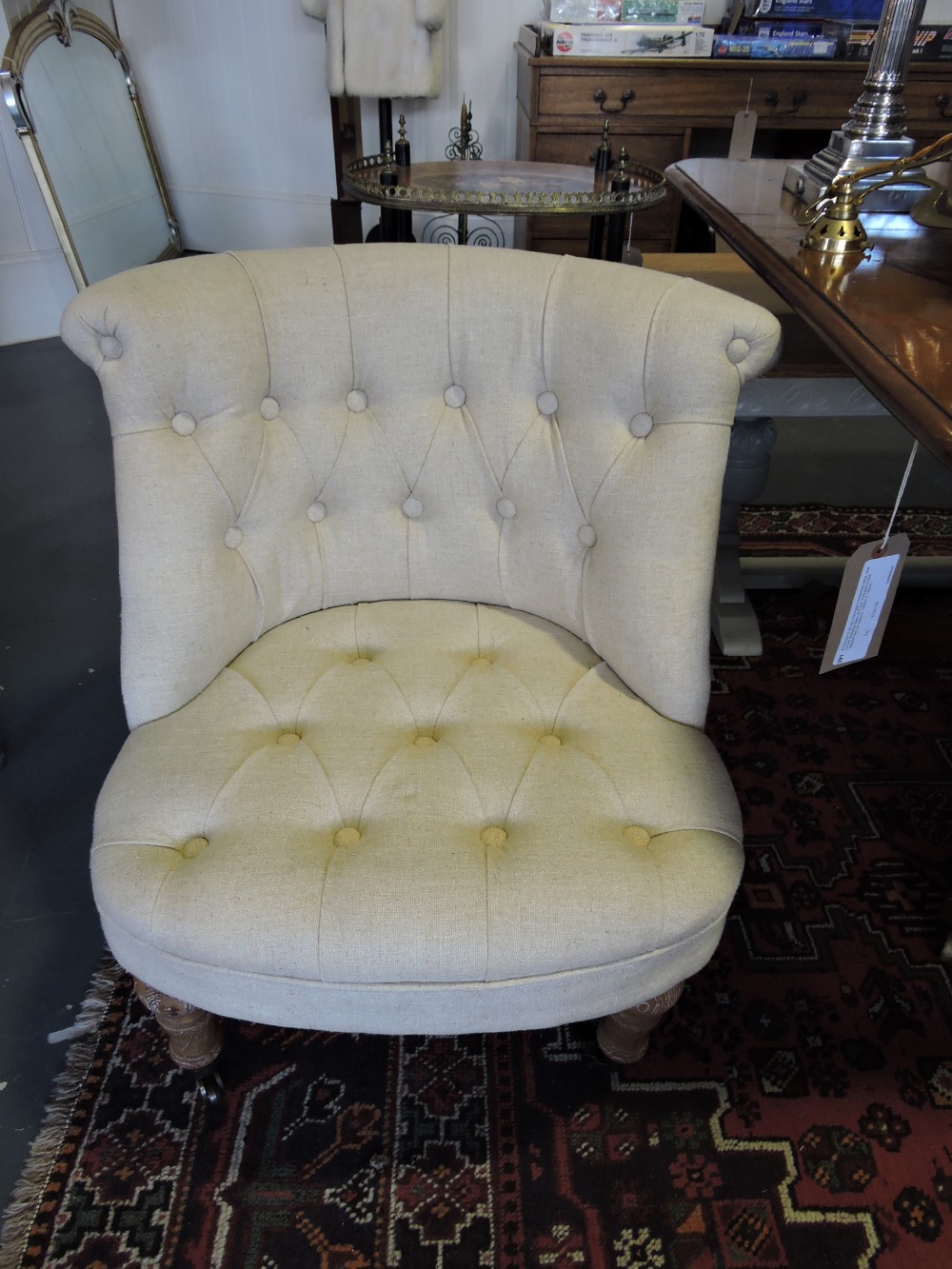 A pair of button upholstered low seat chairs, covered in a natural cotton fabric.