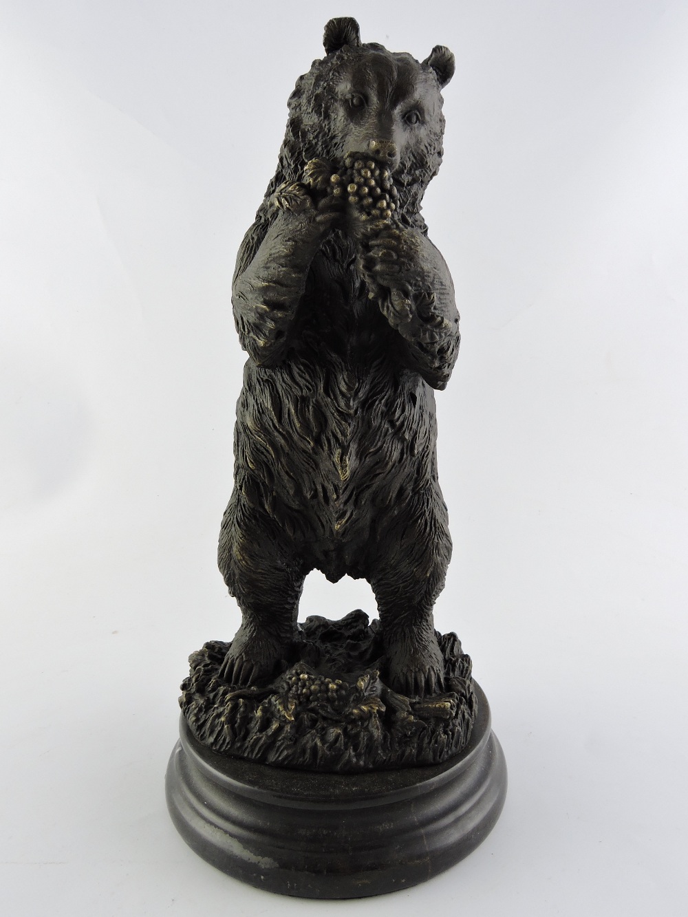 A bronze cast model of a bear, standing on hind legs eating grapes, on a circular marble base, H.