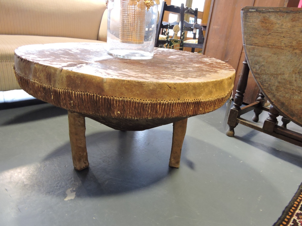 A circular table designed as a tribal drum, with hide covering and wooden supports, D. 81cm.