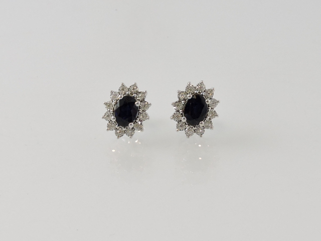 A pair of sapphire and diamond cluster ear studs, the oval sapphire with a band of claw-set diamonds