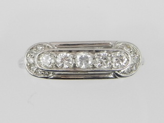 A white metal diamond set dress ring in the Art Deco style, set five brilliant cut stones flanked by