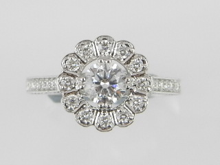 A white metal diamond cluster ring fashioned as a flower head and centred with a brilliant cut
