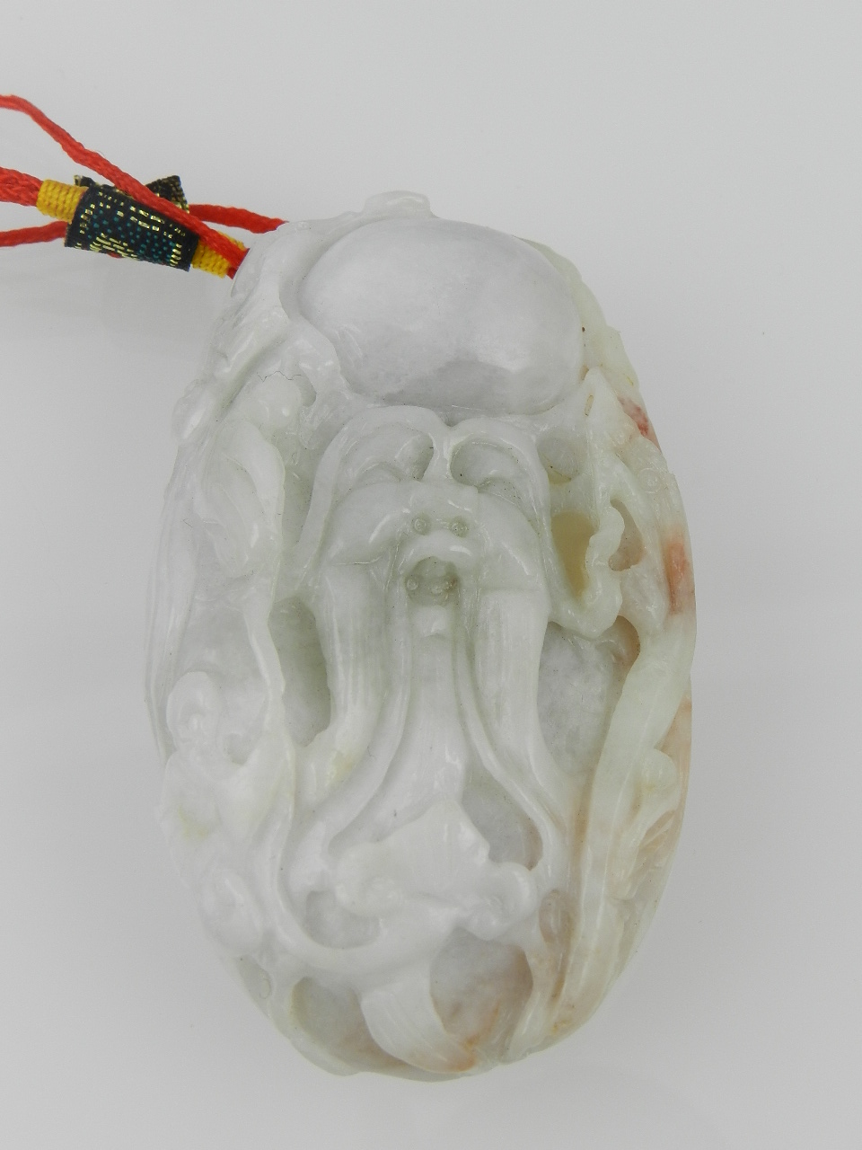 A pale grey / white carved jadeite pendant, relief carved with a mask of a ghost. L: 8.5cm
