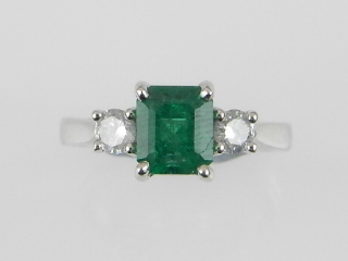 A white metal three stone emerald and diamond ring, the emerald of approx. 1.48cts flanked by two