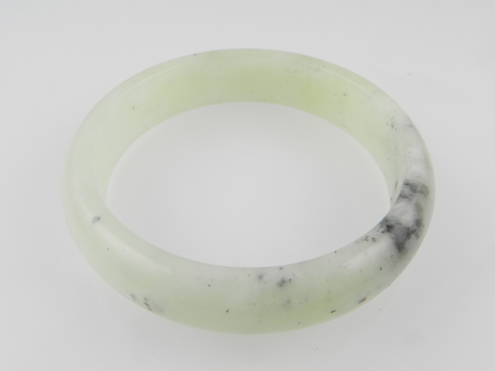 A mottled pale grey-green jadeite bangle. External diameter 7.5cm