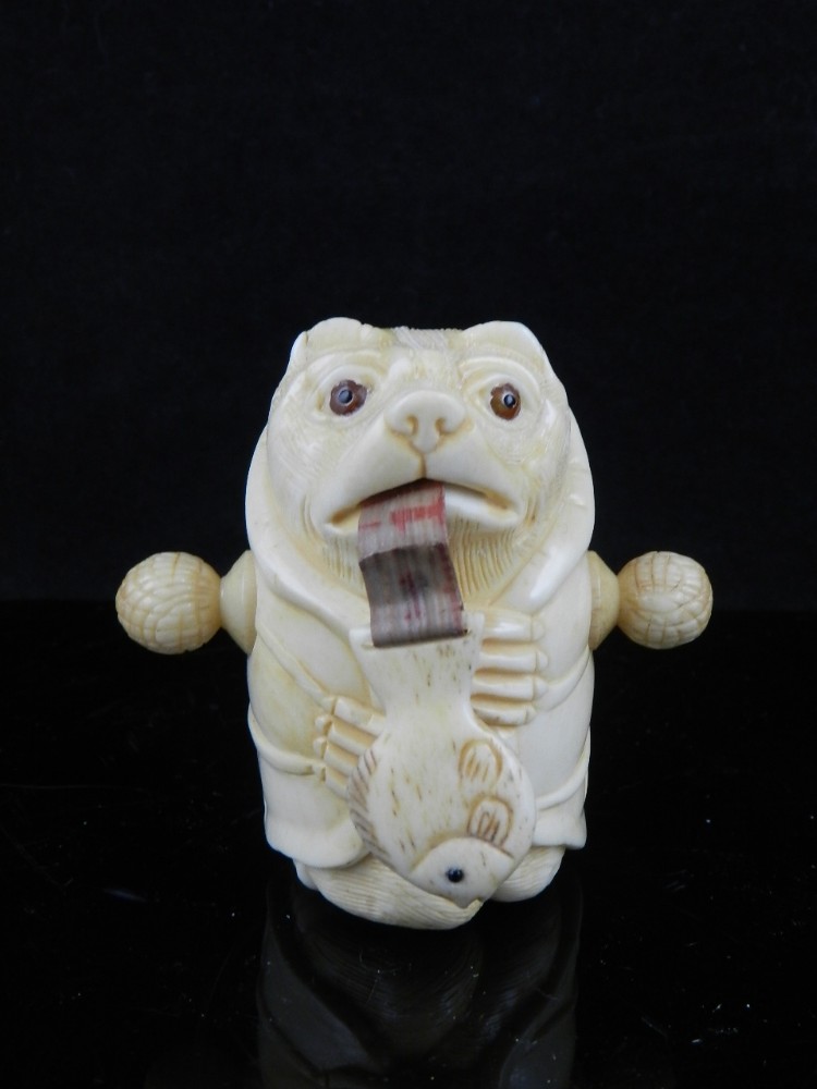 An unusual novelty carved bone tape measure, fashioned as a bear eating a fish. H: 6cm