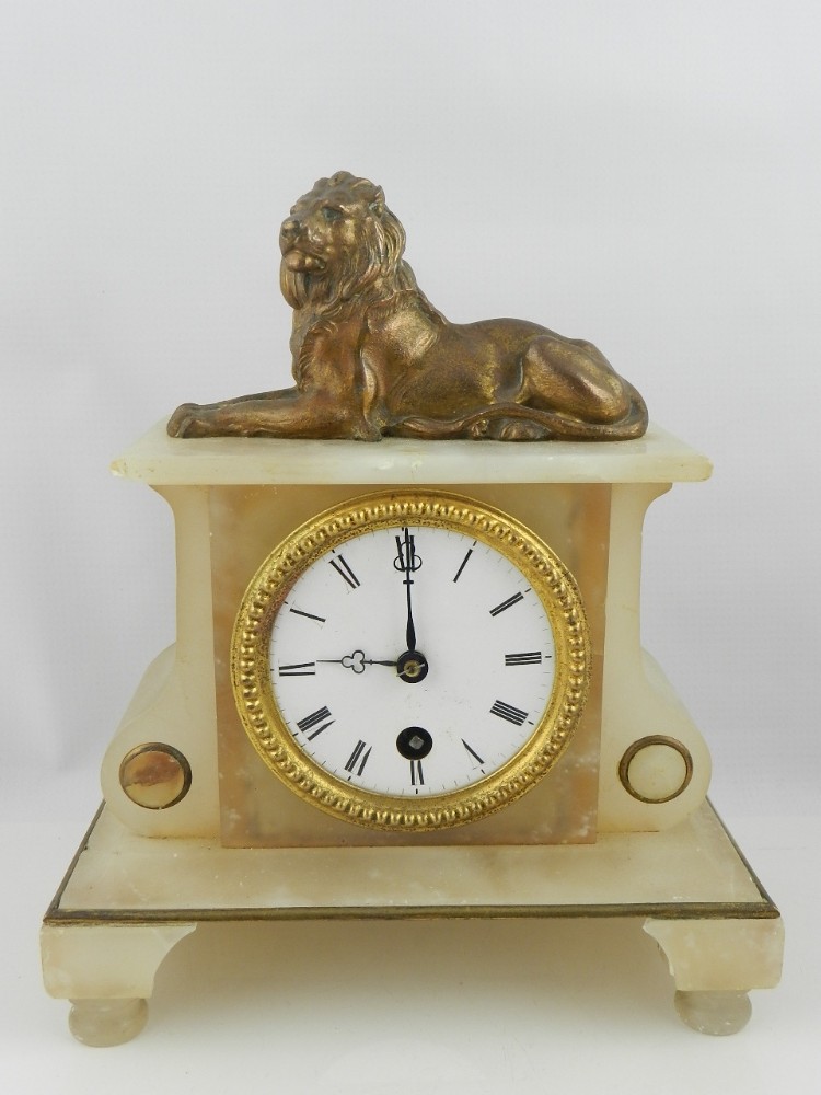 A 19th century French alabaster mantel timepiece, the architectural case surmounted by a recumbent