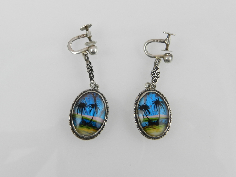 A pair of white metal and butterfly wing drop earrings decorated with palm trees.