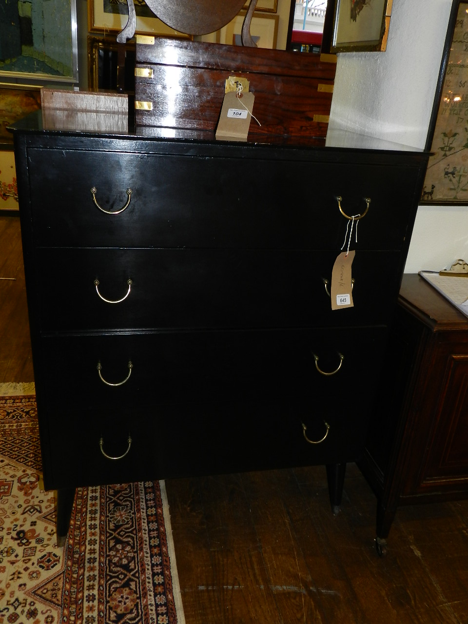 A contemporary ebonised chest of four drawers raised on tubular supports and brass feet.