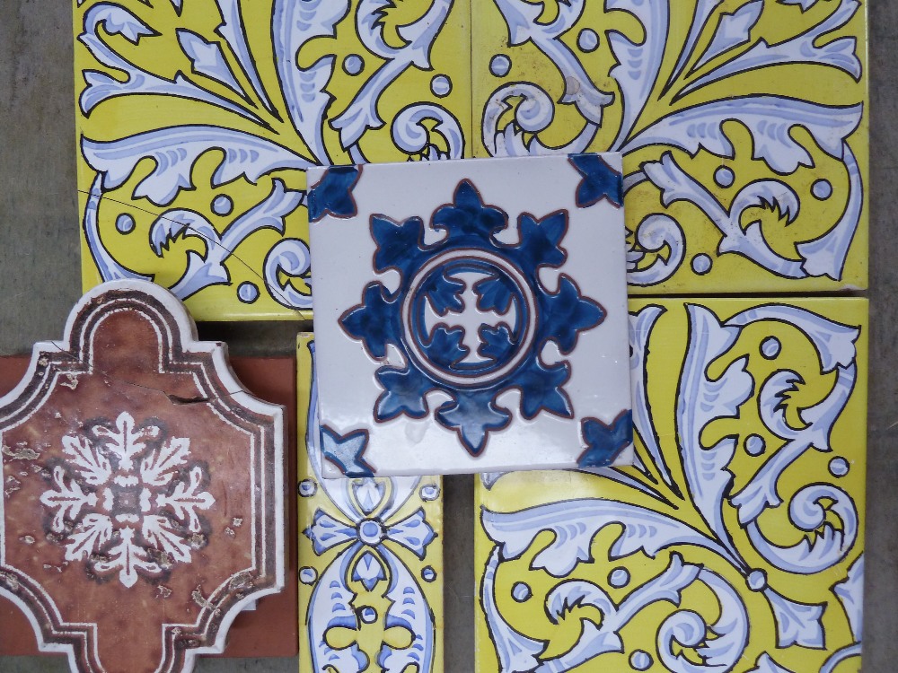 A quantity of terracotta tiles to include three Spanish faience tiles decorated with a bright yellow