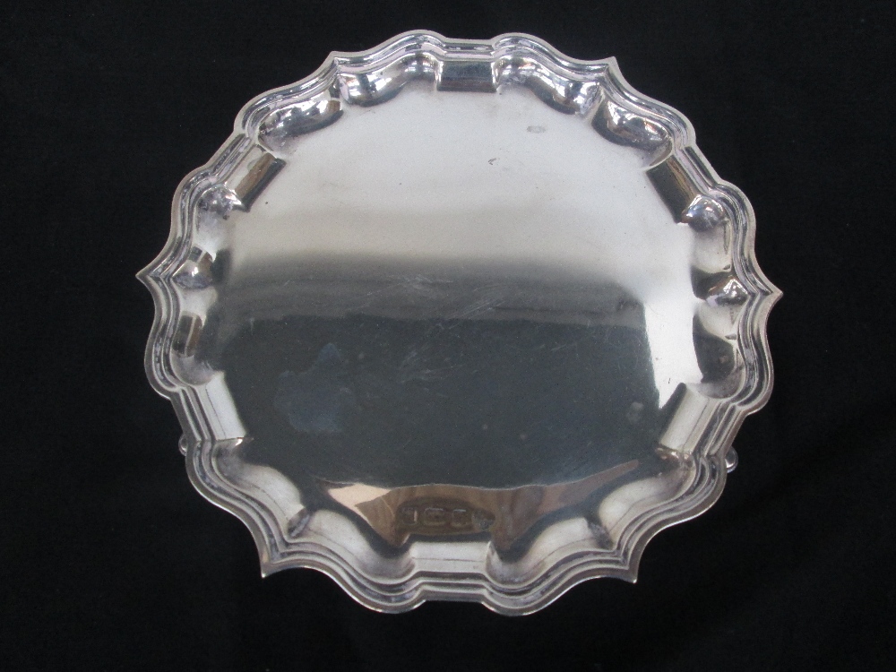 A silver hallmarked charger, by Elkington & Co, scrolling rim, raised on three pedestall feet, marks