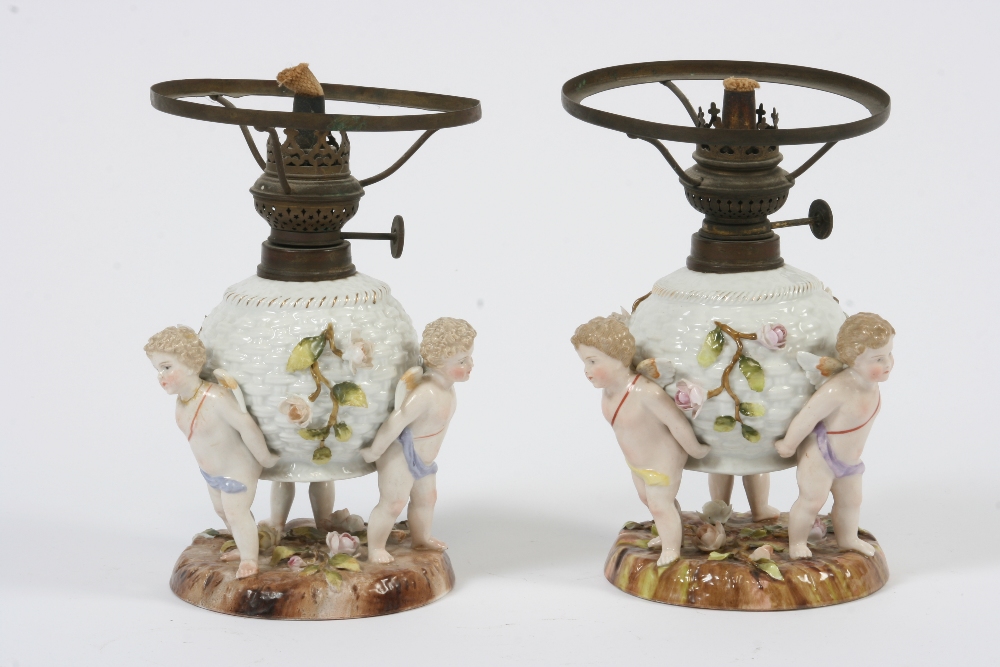 A pair of 19th Century German porcelain cherub decorated table oil lamps, 22.5cm high overall -