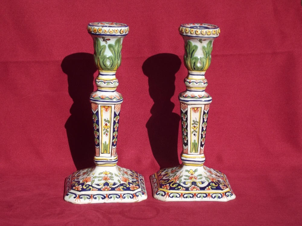 A pair of faience ware candle sticks, raised on square bases, having brightly coloured decoration of