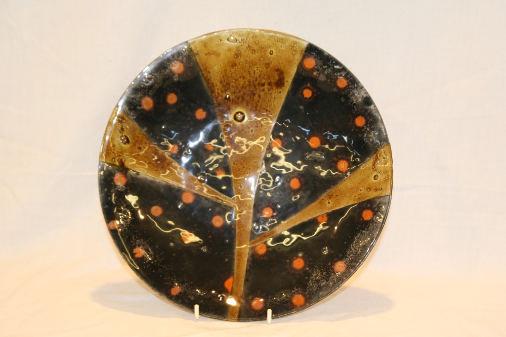 A layered glass circular dish, with colours of amber and orange spots on black ground, 32cm diameter