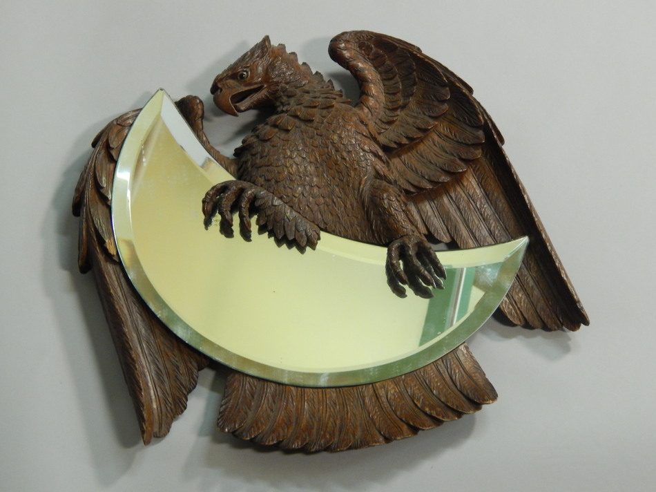 A late 19thC / early 20thC Black Forest wall mirror, carved in the form of an eagle holding a