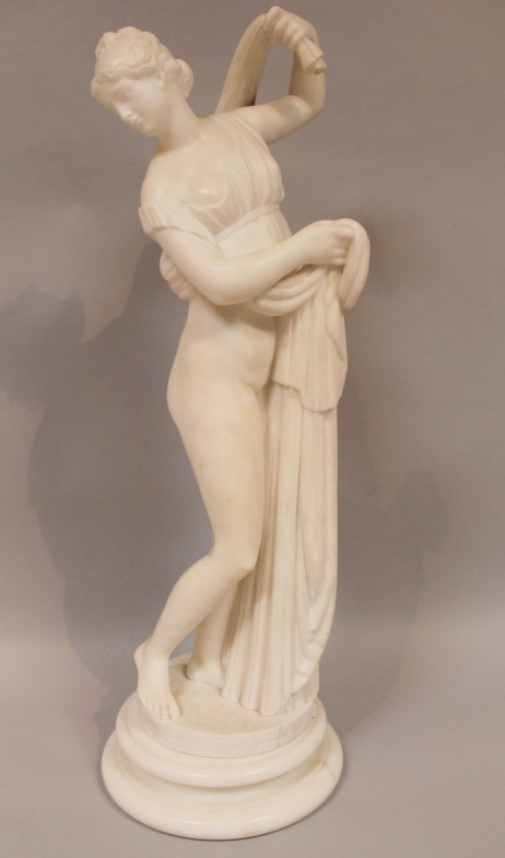 A mid 19thC alabaster figure of a semi clad maiden, dressed in part flowing robes, on a circular