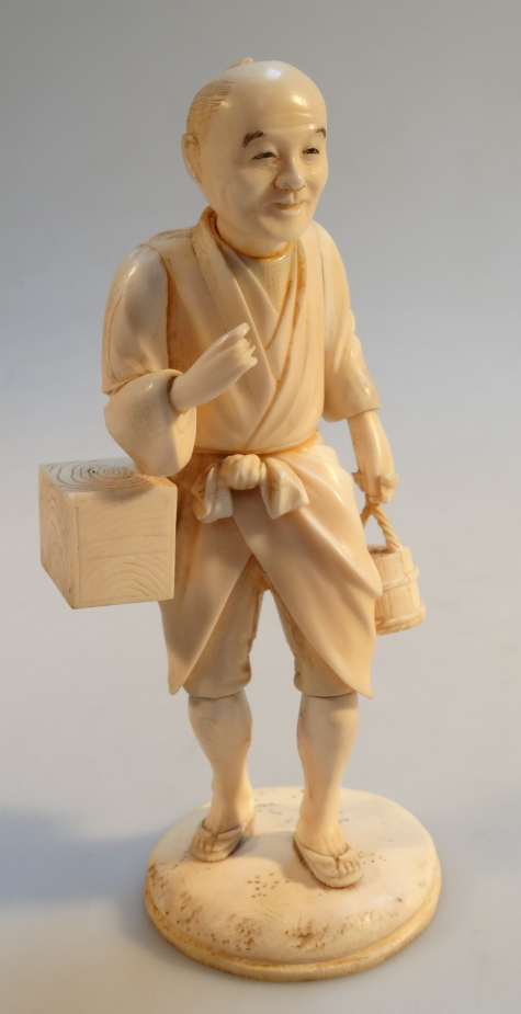 A Japanese ivory okimono, formed as a gentlemen holding a basket and a bento on a shaped base, Meiji