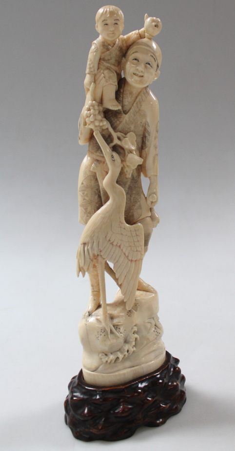 A Japanese carved ivory okimono figure, of a gentleman holding his child aloft, with stork after