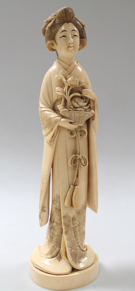 A Japanese carved ivory okimono figure, of a Geisha dressed in kimono holding basket of flowers to