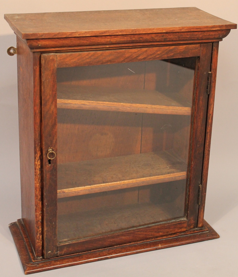 An Edwardian oak hanging cupboard, of rectangular form, the hinged glazed door revealing removable