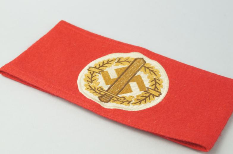 A Third Reich SA Wehrmannschaft arm band, in red felt with central cream sewn swastika with dagger