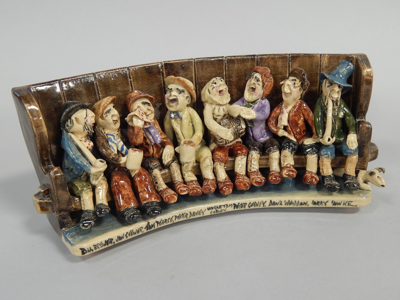 A Will Young Uncle Tom Cobley pottery group, of figures seated on a settle, signed Will Young,